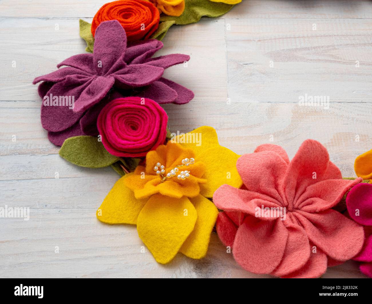 Primo piano di colorate ghirlande di fiori di feltro fatte a mano su sfondo in legno lavato di lime. Foto Stock