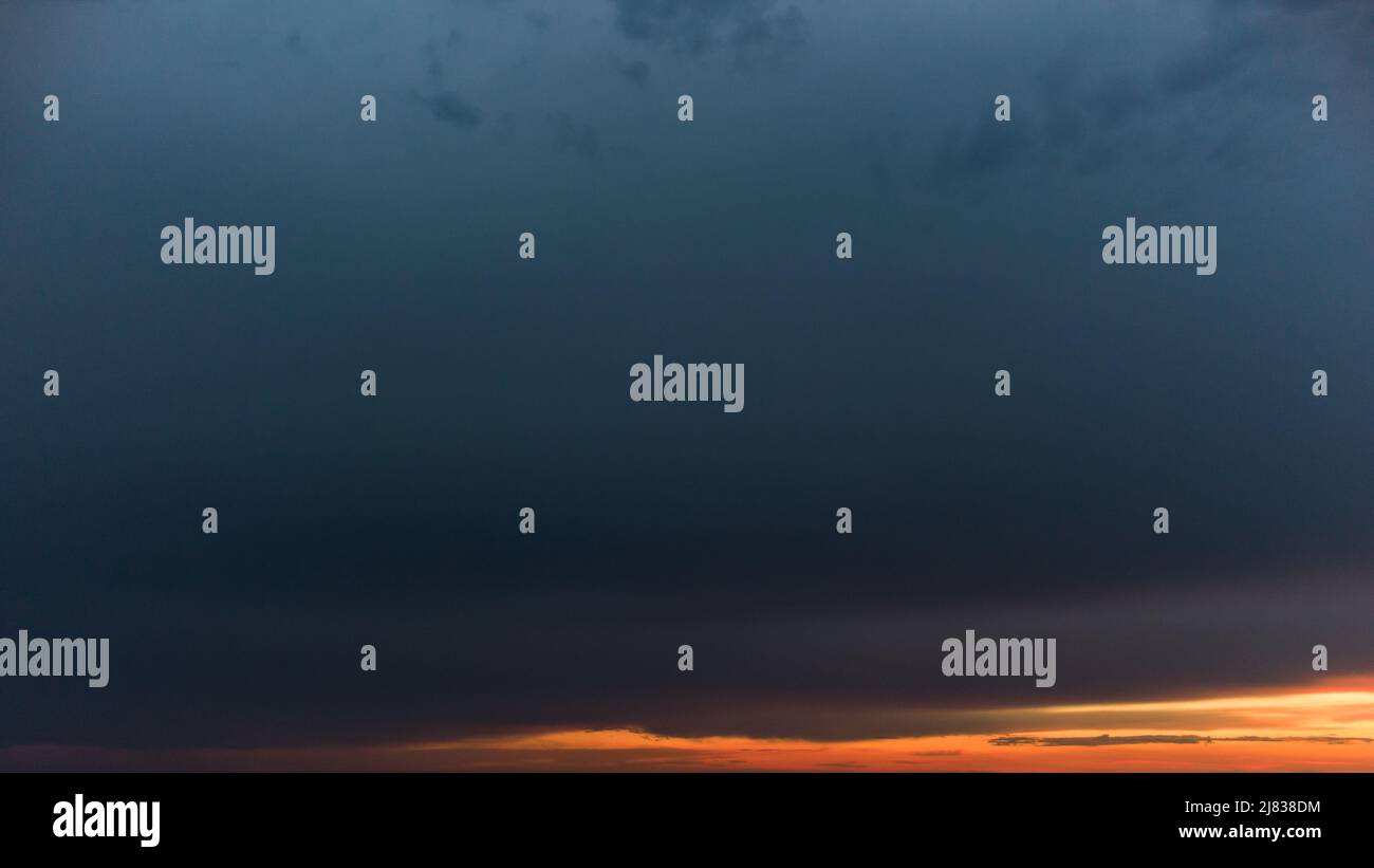 Ampia vista panoramica aerea, epica vista del paesaggio nuvoloso scuro sopra gli strati vividi del tramonto arancione. Nuvole blu pesanti che coprono la colorata scena del cielo serale Foto Stock