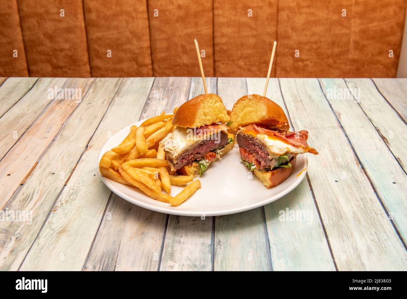 Delizioso hamburger di manzo cotto in stile americano con uova fritte, pancetta, lattuga, pane brioche e una porzione di patatine fritte Foto Stock