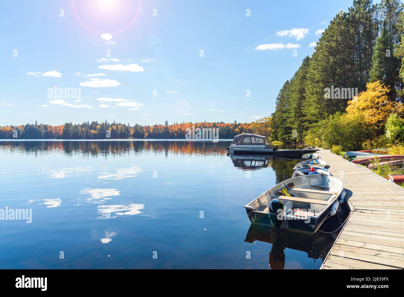 Piccole barche ormeggiate ad un molo di legno su un lago beutiful circondato da una foresta decidua in un giorno d'autunno soleggiato. Lente svasata e caduta fogliame. Foto Stock
