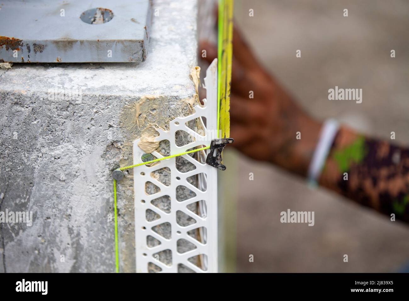 un operatore edile che misura la larghezza di una colonna di calcestruzzo per la bordatura angolare come preparazione per l'applicazione in stucco Foto Stock