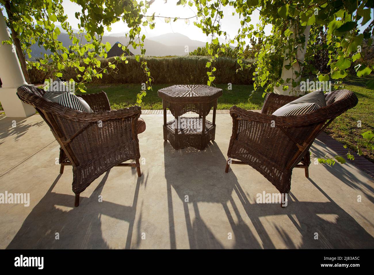 Sedie in vimini e Table Casting Long Evening Shadows alla fattoria la cotte Foto Stock