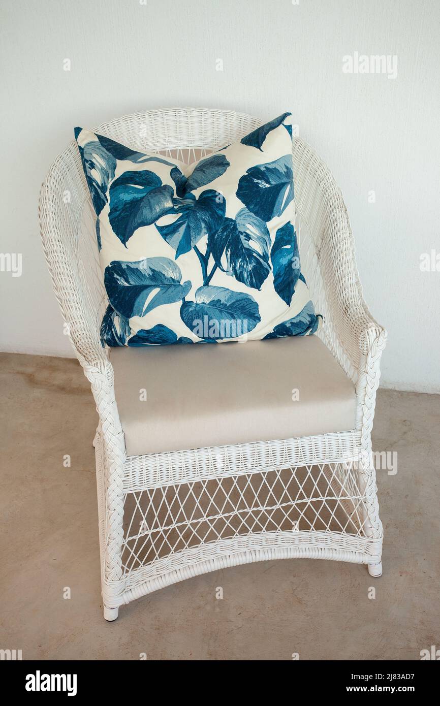 Sedia in vimini bianca con un audace cuscino in foglia blu Foto Stock