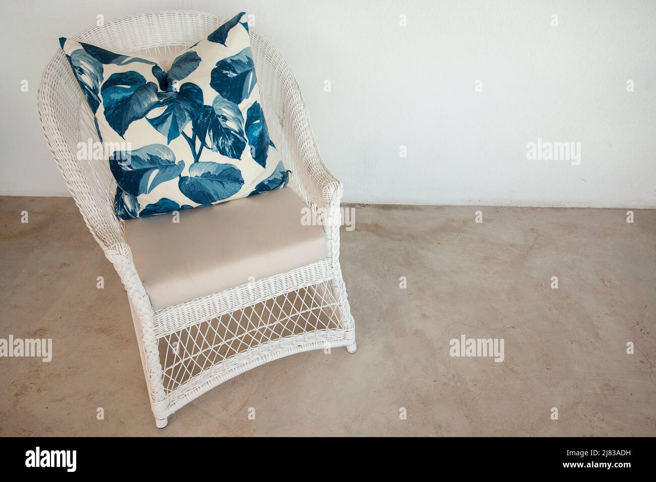 Sedia in vimini bianca con un audace cuscino in foglia blu Foto Stock
