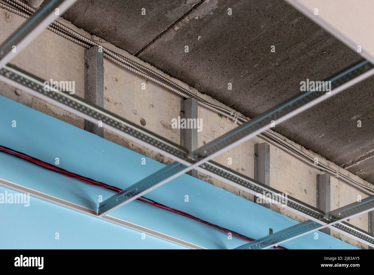 installato inferiore acciaio zincato tegole quadrate goccia giù soffitto con cartongesso verniciato, esponendo cornice di metallo dietro la cartongesso. Questa è una classe scolastica. Foto Stock