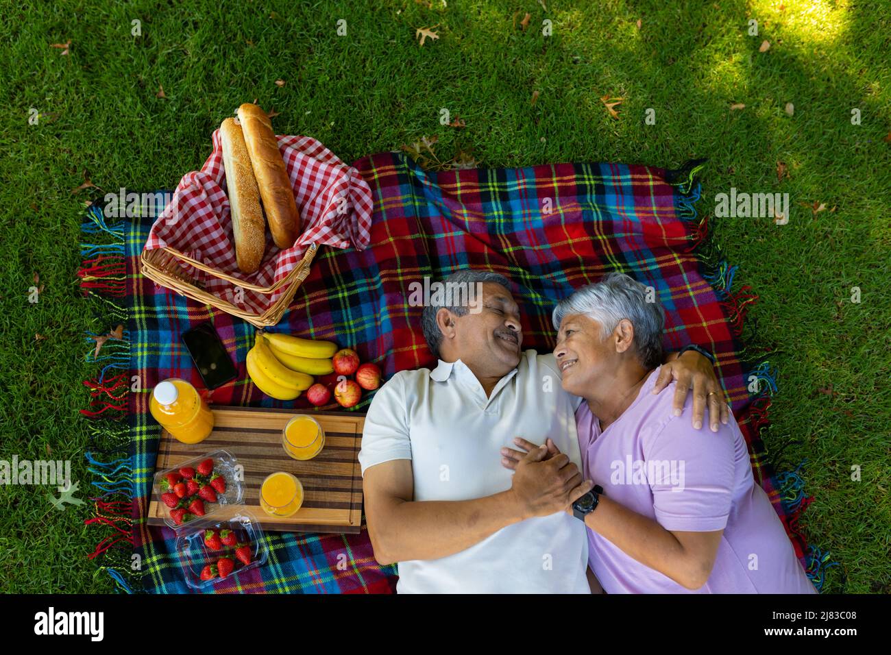 Vista ad alto angolo di coppia sorridente biraciale con cibo e bevande sdraiati su coperta nel parco Foto Stock