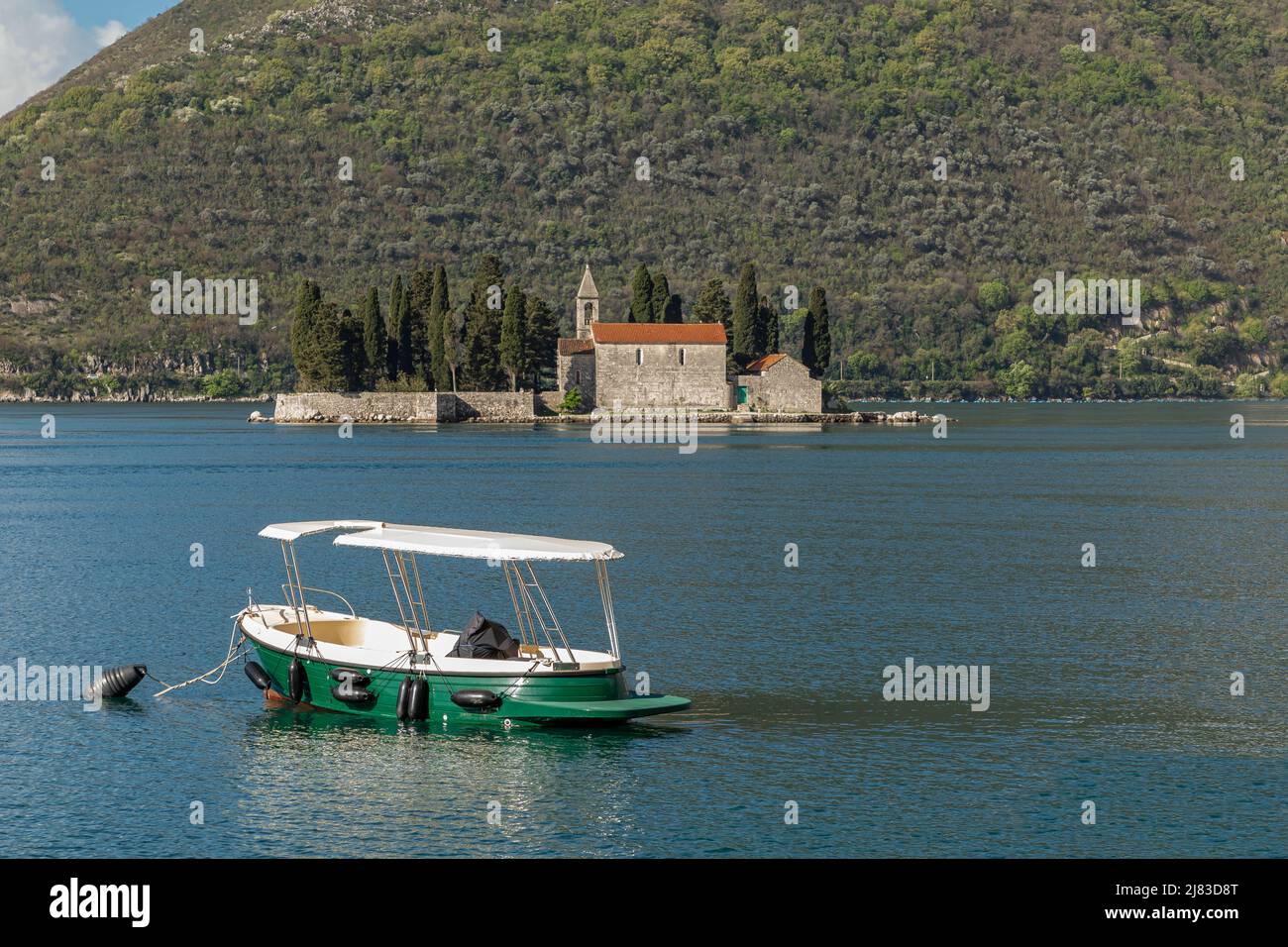 Barca ormeggiata nel mare in Bosnia Erzegovina con una chiesa a base di isola sullo sfondo Foto Stock