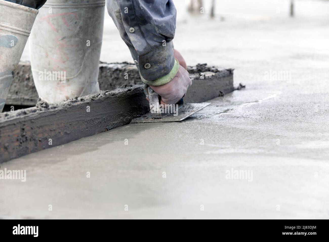 Costruzione che lavora con il suo edger in acciaio per spianare gli angoli di una soletta di calcestruzzo appena versata di un edificio residenziale. Foto Stock