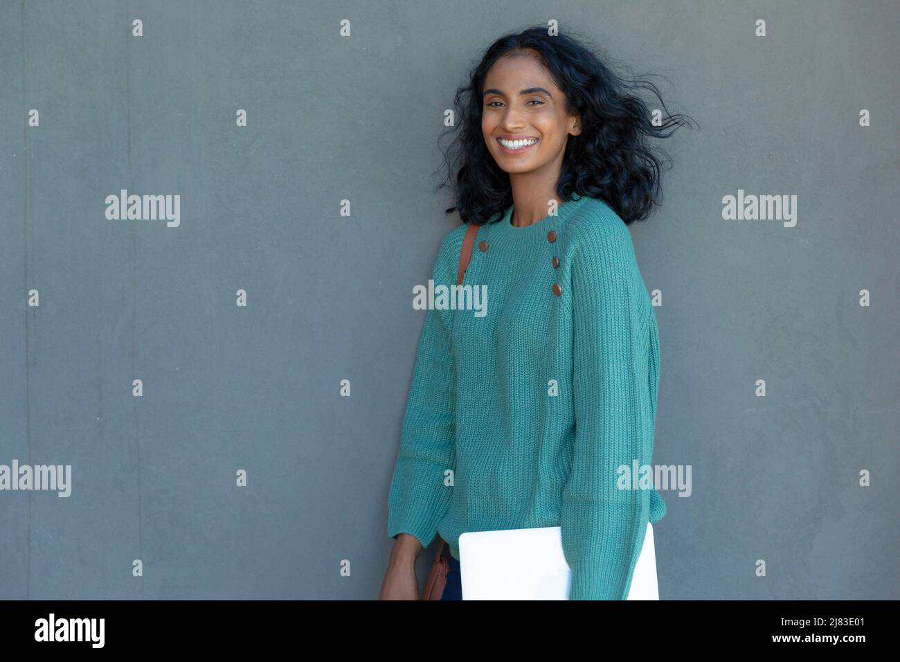 Felice giovane donna d'affari biraciale bella con PC tablet in piedi contro parete grigia sul posto di lavoro Foto Stock