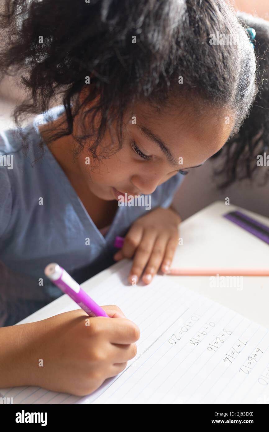 Primo piano della studentessa biraciale elementare che risolve le somme di matematica sul libro alla scrivania in classe Foto Stock