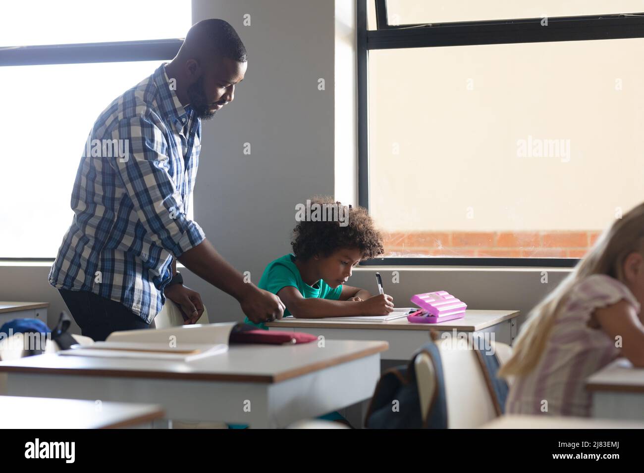 Insegnante di giovani maschi afroamericani che assiste il ragazzo della scuola elementare afroamericana che studia alla scrivania Foto Stock