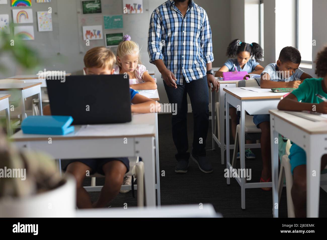 Metà della sezione del giovane insegnante maschile afroamericano che cammina da studenti multirazziali che studiano in classe Foto Stock