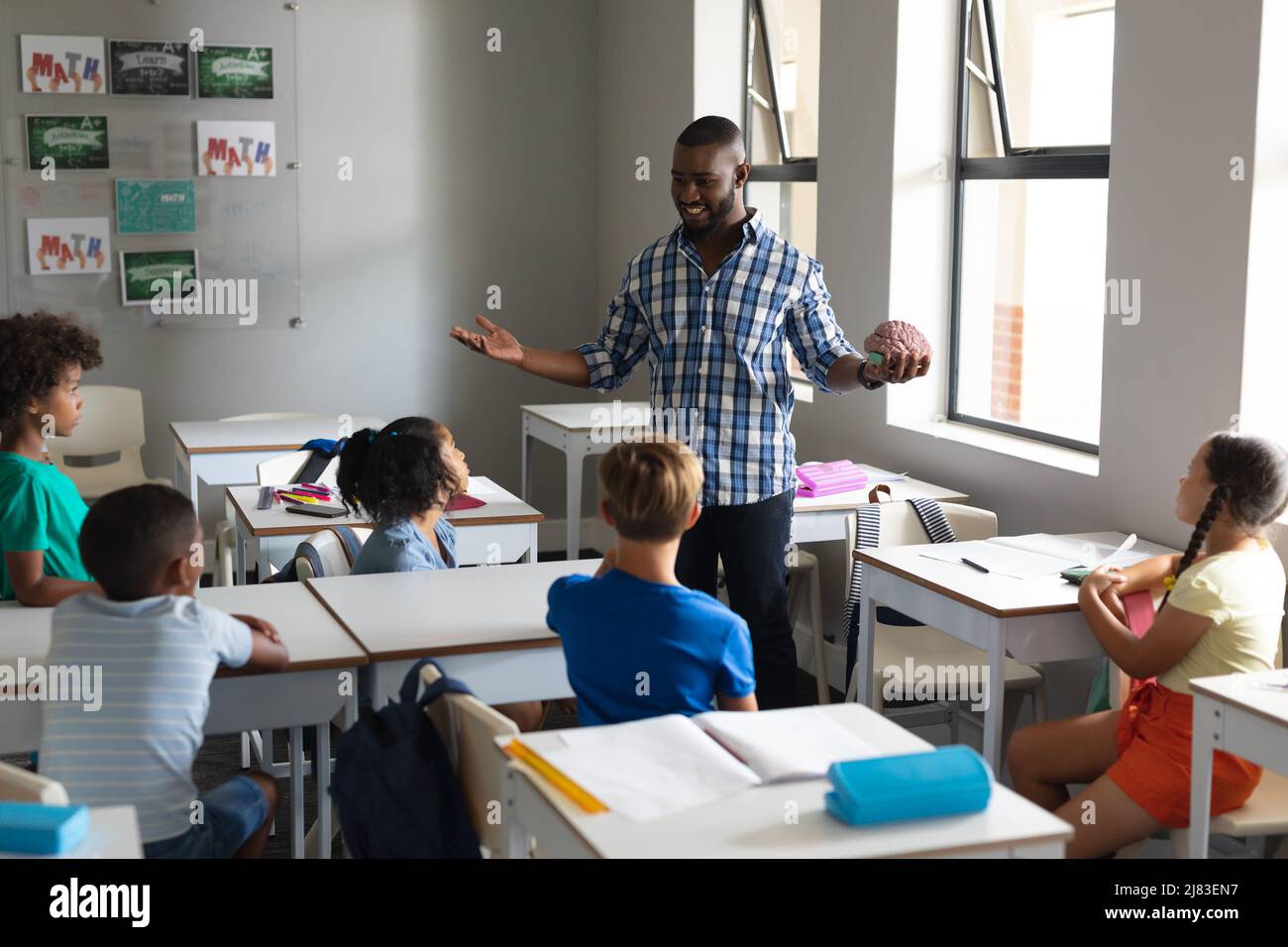 Sorridente insegnante di giovani maschi afroamericani che mostra il modello del cervello agli studenti elementari multirazziali Foto Stock