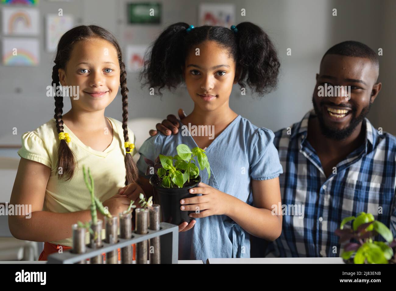 Ritratto di scolaresche biraciali elementari con pianta in piedi da giovane insegnante afroamericano Foto Stock