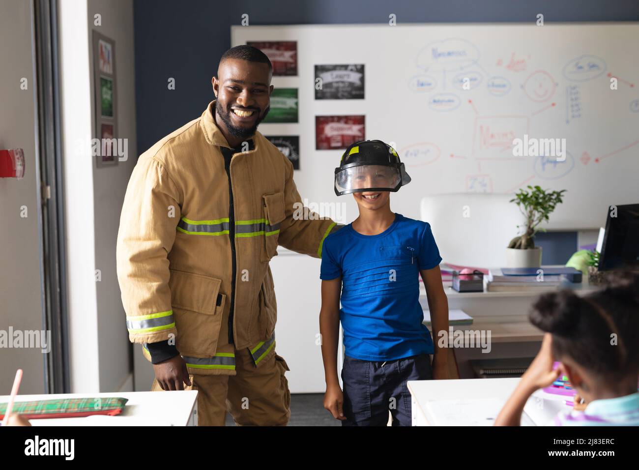 Insegnante maschile africano americano giovane con ragazzo elementare caucasico che indossa casco protettivo in classe Foto Stock