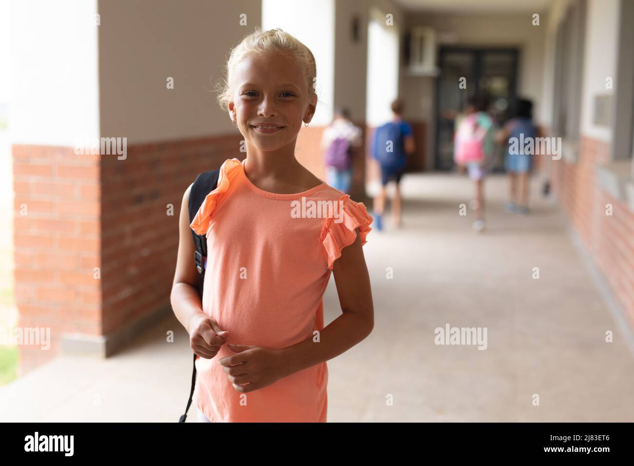 Ritratto di sorridente scolaretta caucasica elementare in piedi nel corridoio Foto Stock