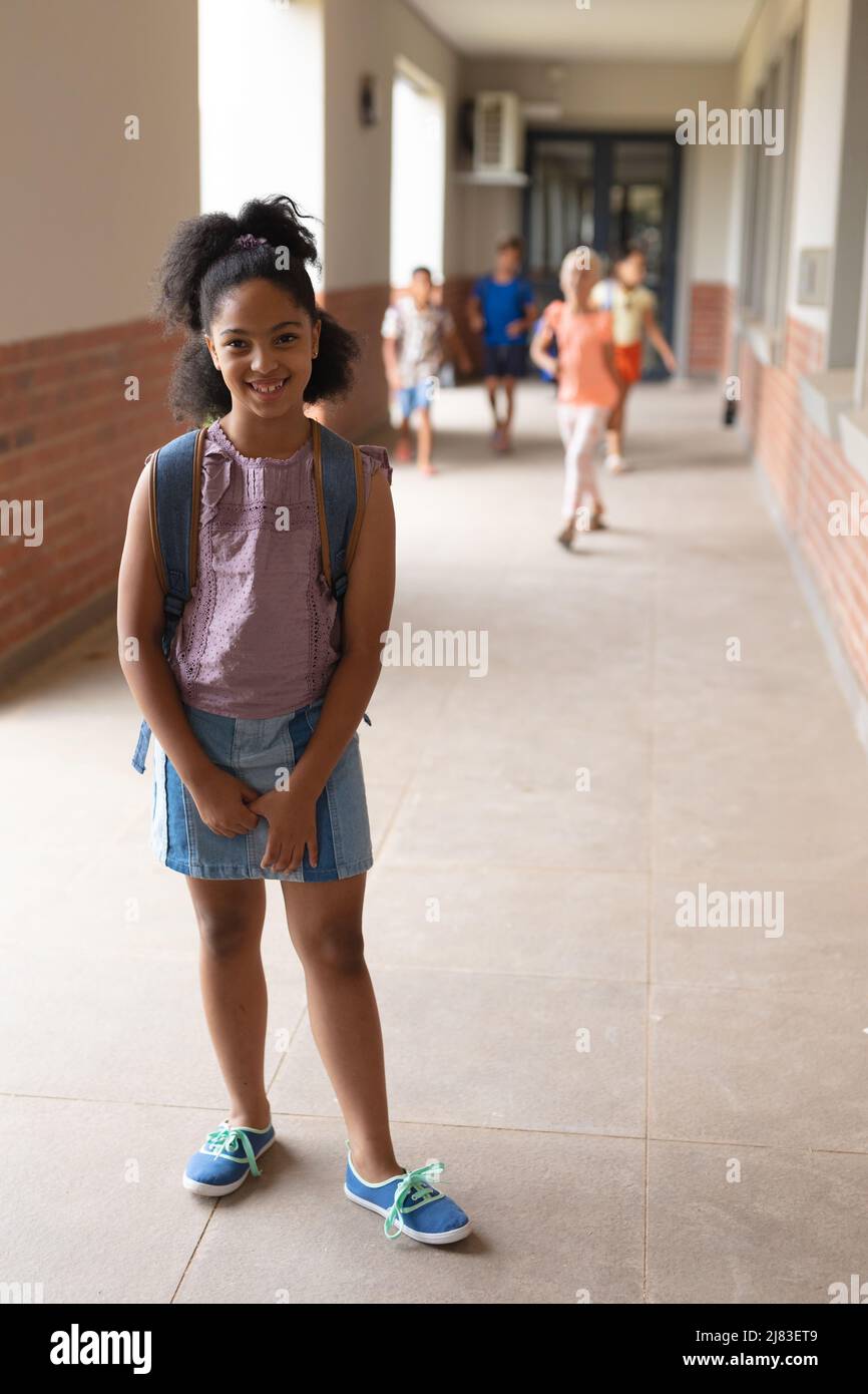 Ritratto di sorridente studentessa biraciale elementare in piedi nel corridoio Foto Stock