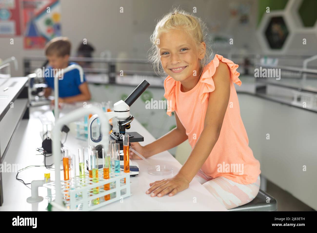 Ritratto di scolaretta caucasica sorridente seduta al microscopio in laboratorio scolastico Foto Stock