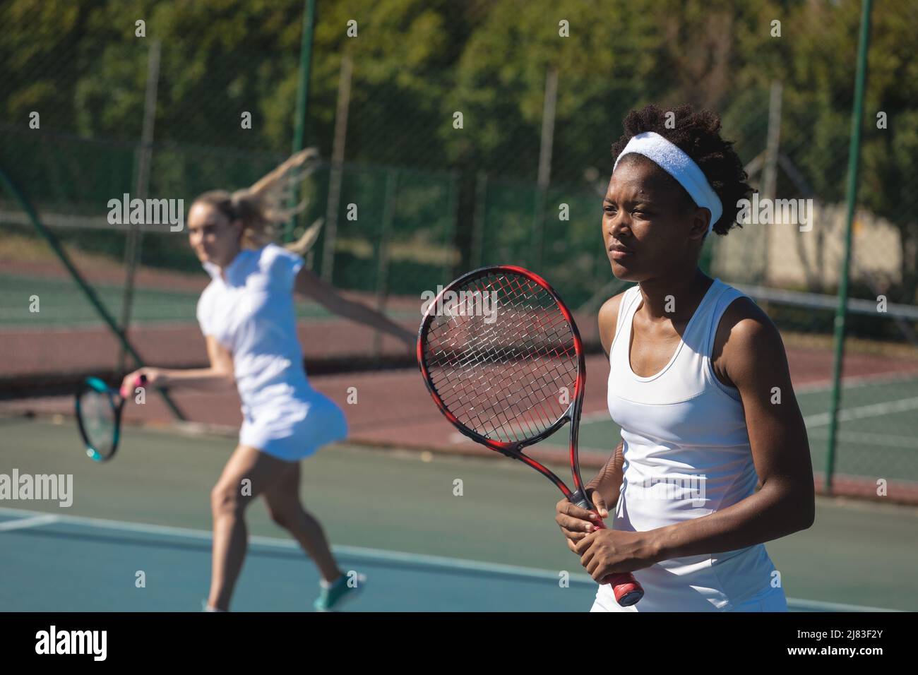 Tennista africano americano femminile giocando con caucasico doppio partner in campo in giornata di sole Foto Stock