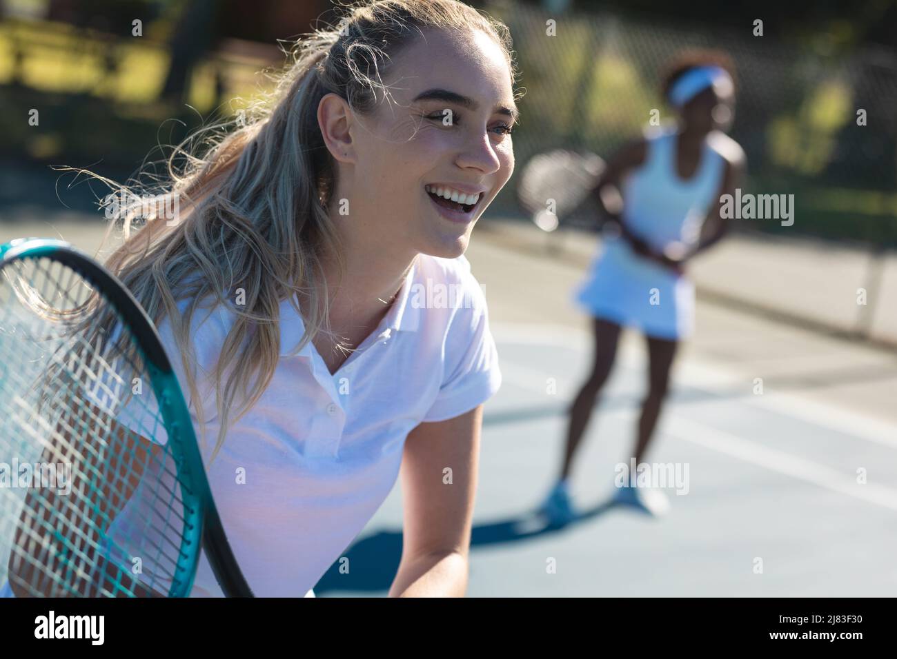 Allegra giovane tennista caucasica con partner afroamericano in campo il giorno di sole Foto Stock
