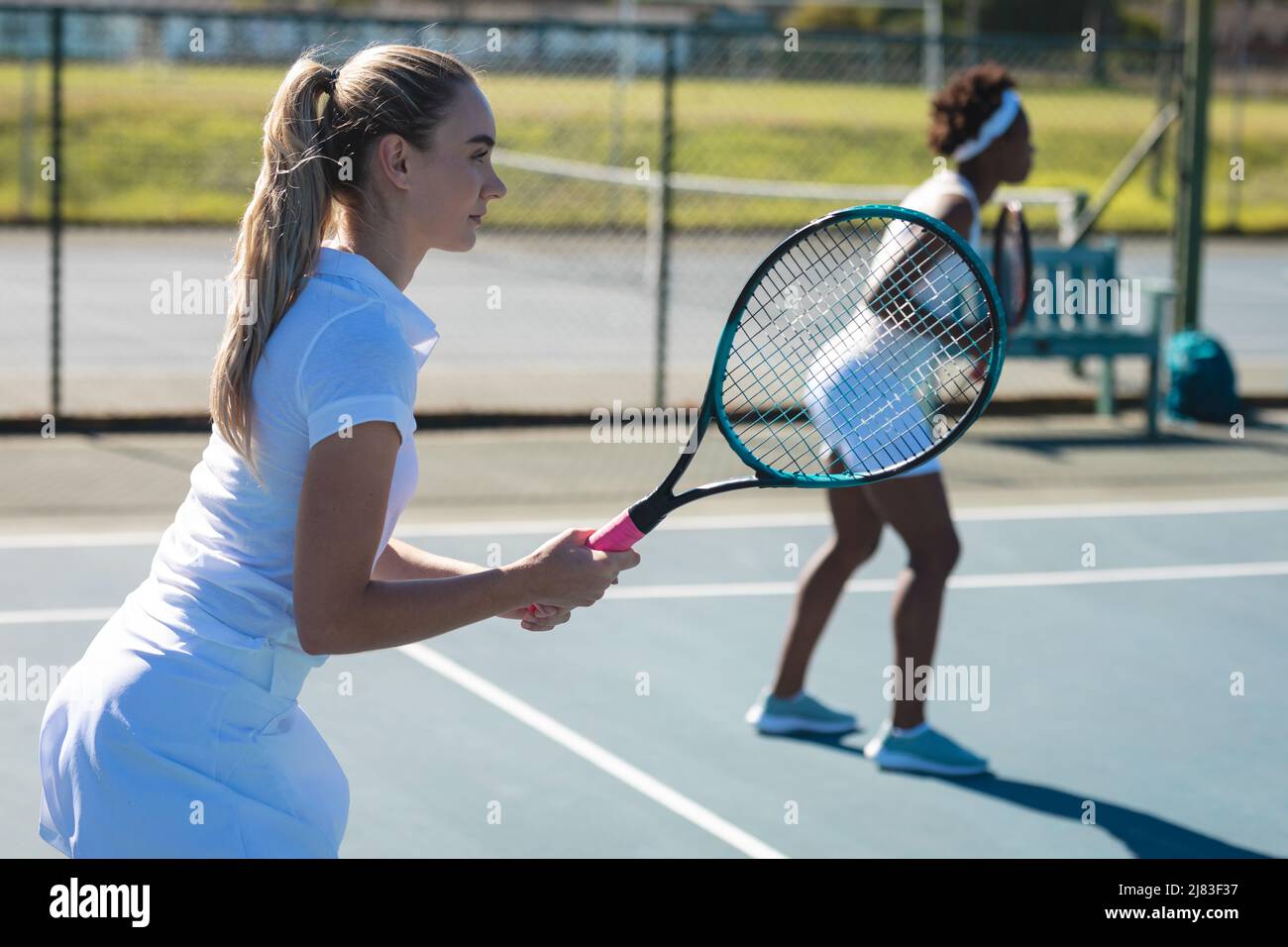 Giocatore femminile caucasico che gioca con partner africano doppio al campo da tennis Foto Stock