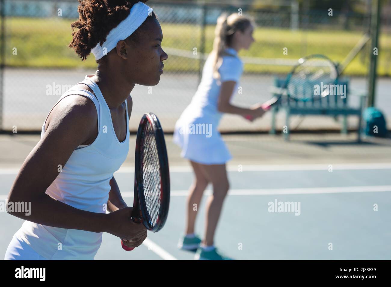 Giocatore femminile afroamericano che gioca a tennis con partner caucasico doppio in campo Foto Stock