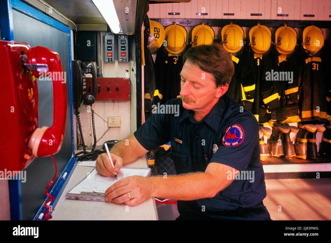 1990S UOMO IN UNIFORME FIREMAN RAPPORTO DI SCRITTURA ALLA SCRIVANIA IN FIREHOUSE ATTREZZATURA DI SICUREZZA CASCHI CAPPOTTI STIVALI PENDENTI IN BACKGROUND - KF29646 NET002 HARS POSTI DI LAVORO CAPPOTTI COMUNICANTE COPIA SPAZIO RAPPORTO MEZZA LUNGHEZZA PERSONE ISPIRAZIONE CURA MASCHI RISCHIO PROFESSIONE VIGILE DEL FUOCO ABILITÀ DI OCCUPAZIONE PROTEZIONE FORZA CORAGGIO CARRIERA ECCITAZIONE LEADERSHIP LAVORO A NEL LAVORO OCCUPAZIONI TELEFONI VIGILI DEL FUOCO TELEFONI CASCHI INFRASTRUTTURA DIPENDENTE UNIFORME FUNZIONARIO PUBBLICO VIGILI DEL FUOCO FUOCHI METÀ-ADULTO METÀ-ADULTO UOMO STAZIONE CASA CAUCASICA ETNIA VIGILI DEL FUOCO DIPARTIMENTO DEL FUOCO FUOCHI D'ARTIFICIO VECCHIO STILE Foto Stock