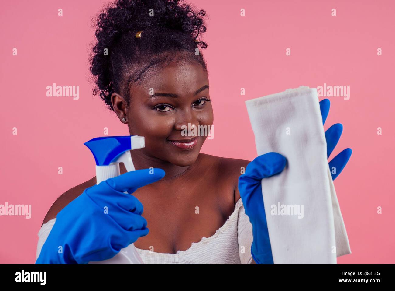 donna che usa lo spray per pulire le pareti rosa backgroung studio Foto Stock