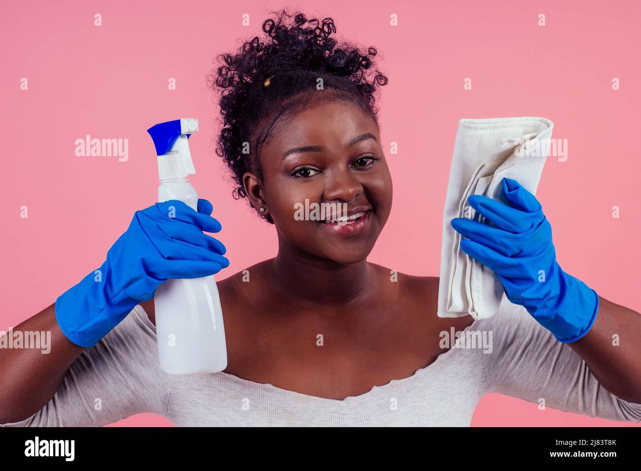 donna che usa lo spray per pulire le pareti rosa backgroung studio Foto Stock