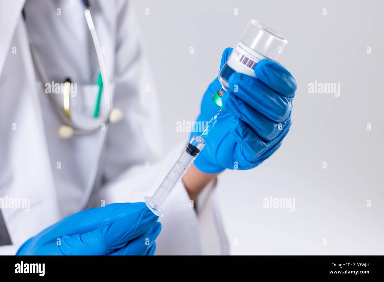 Sezione centrale di donna di metà adulta afroamericana che indossa guanti che tengono il flaconcino e la siringa Foto Stock