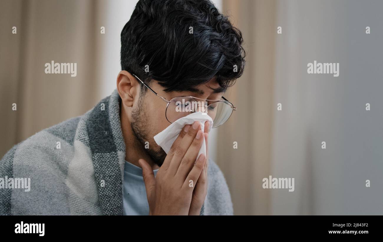 Primo piano triste arabo esausto uomo ported affetto da allergia stagionale virus della polvere malattia respiratoria naso runny ragazzo in occhiali avvolti in coperta Foto Stock
