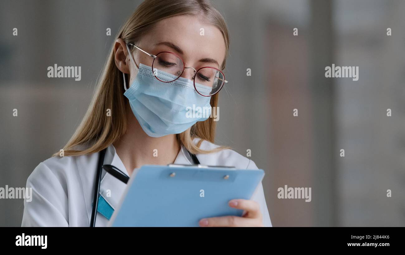 Ritratto donna caucasica medico infermiere in maschera medica di protezione scrivere informazioni nel giornale di registrazione medica femmina in terapia occhiali Foto Stock