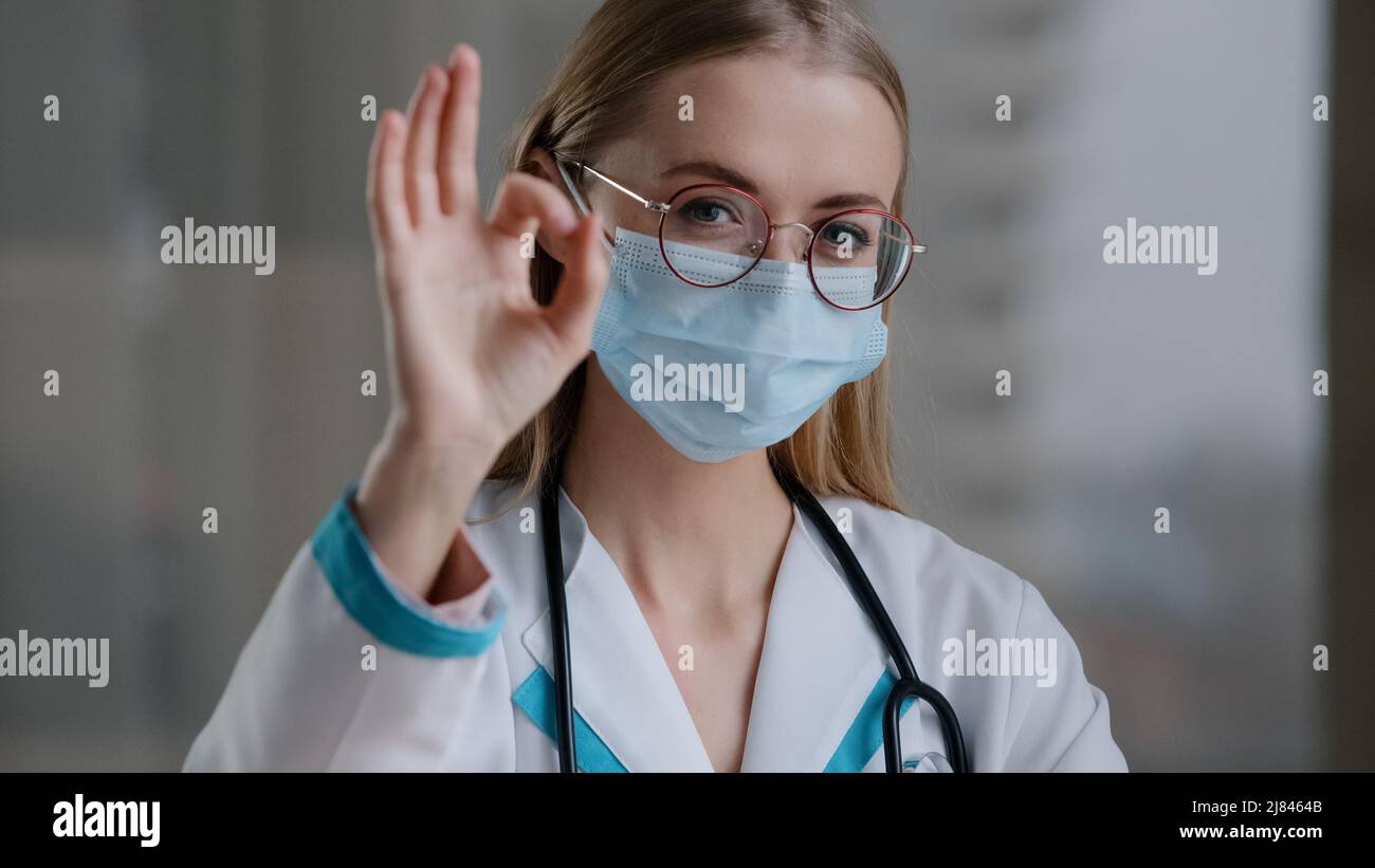 Ritratto medico caucasico specialista terapista infermiere chirurgo donna ragazza in occhiali in maschera medica di protezione del viso guardando la macchina fotografica che mostra ok Foto Stock