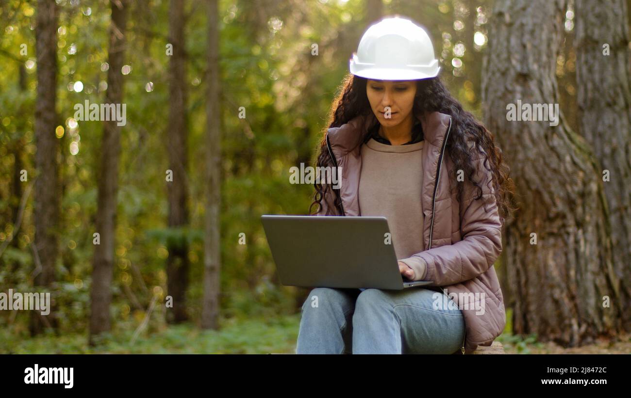 Donna millennial giovane esperto specialista forestale ingegnere tecnico ambientalista in hardHat controllo alberi immissione dati in laptop prendere Foto Stock