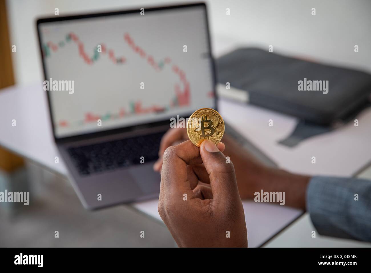 Primo piano di una moneta bitcoin tenuta in mano da un investitore, crash di mercato e grafico negativo in rosso, crisi finanziaria e concetto di inflazione Foto Stock