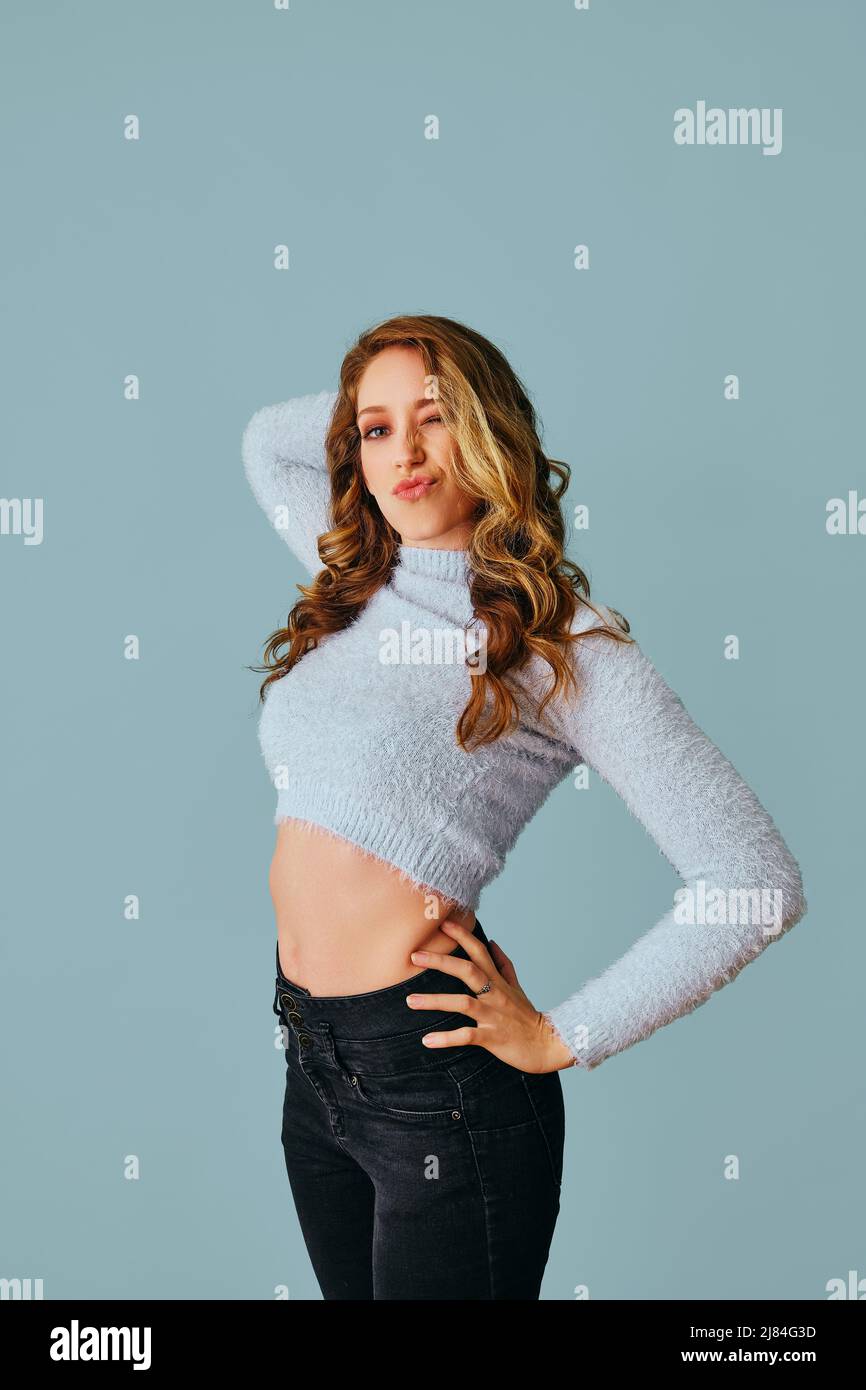 bella giovane donna che indossa un maglione e jeans su sfondo grigio studio ritratto flirting soffiante bacio Foto Stock