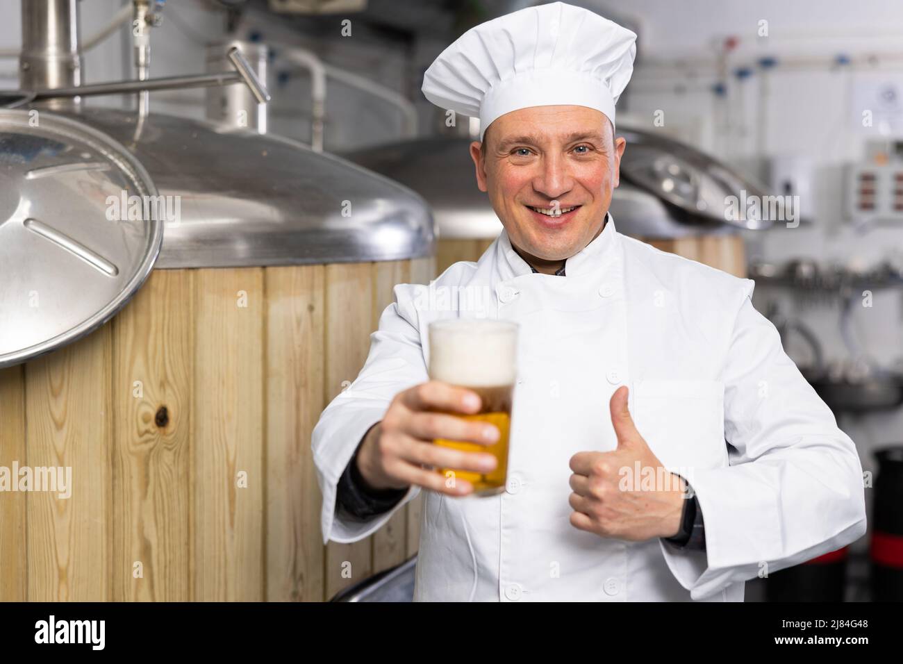 Ritratto del birrificio che sta in piedi con un bicchiere di birra sul suo posto di lavoro in birreria Foto Stock