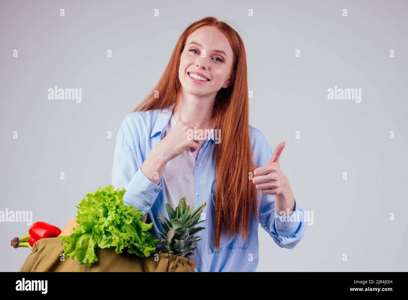 bella donna zenzero redhaired tenuta eco borsa di cotone shopper con frutta fresca, verdura, mostrando pollici in su in wgite studio sfondo Foto Stock