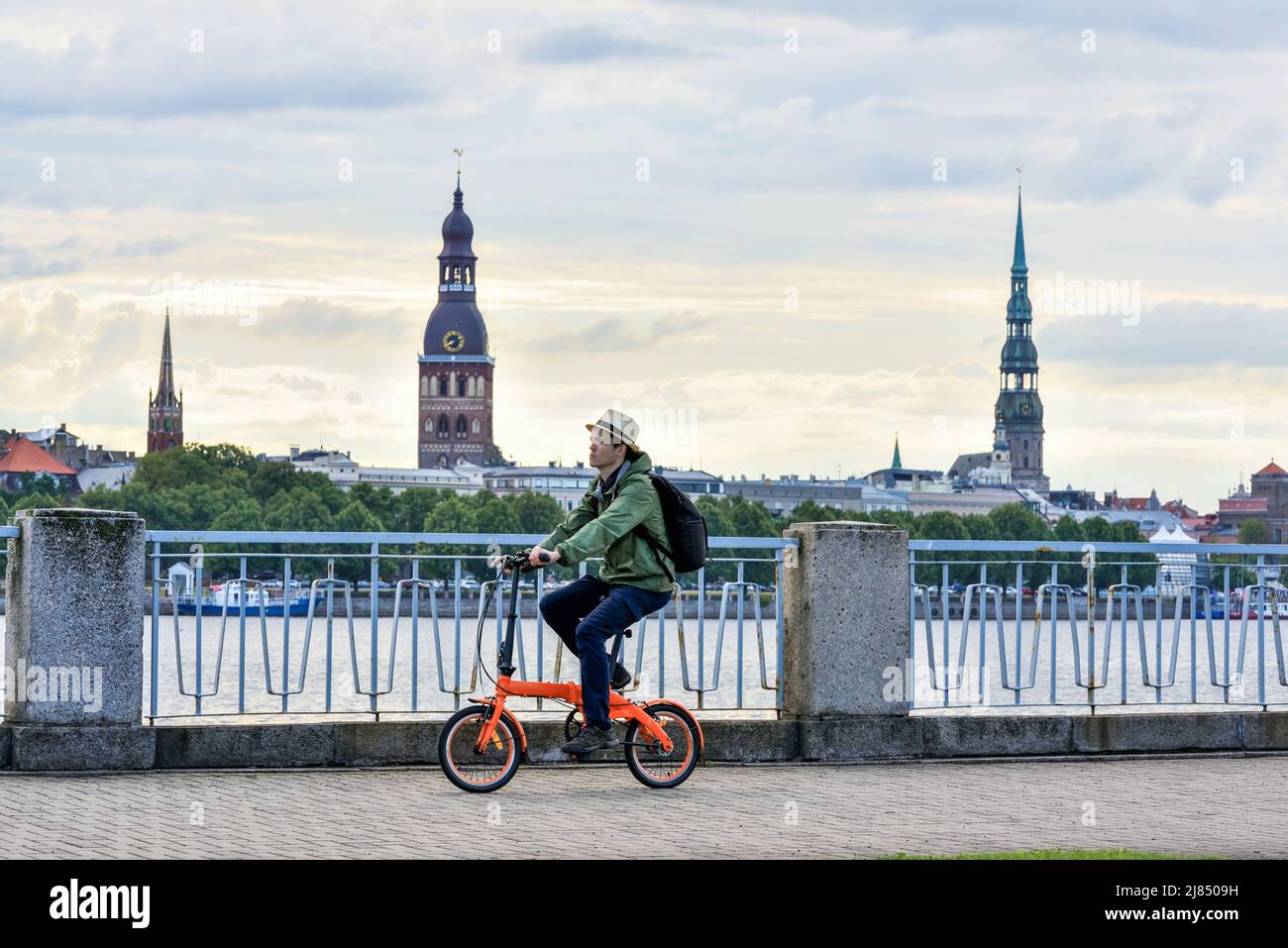Un ciclista fa un giro in bicicletta vicino al fiume Daugava sullo sfondo della città vecchia di riga, Lettonia. Bicicletta in città Foto Stock