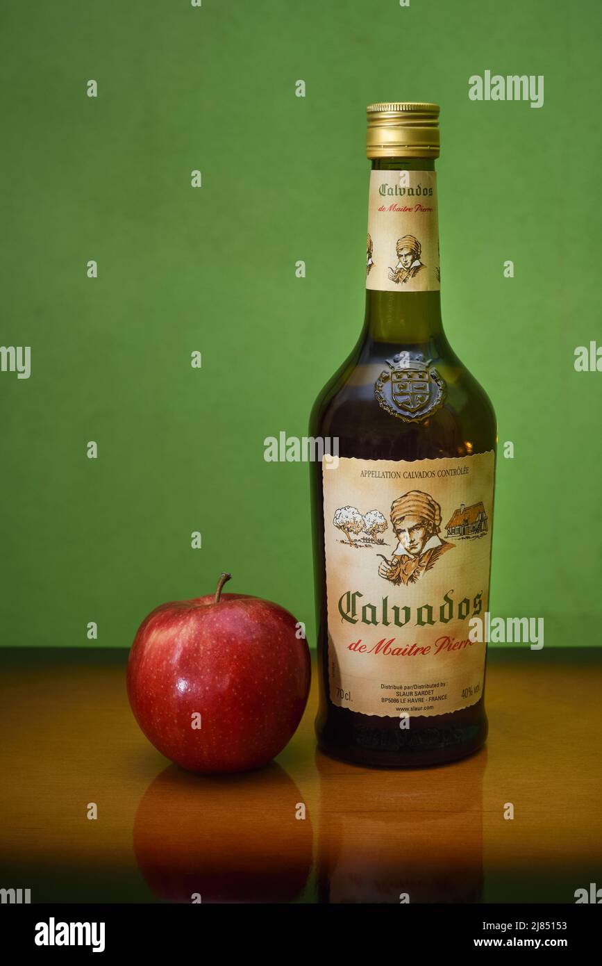 Bottiglia di brandy calvados e una mela su un tavolo di legno su sfondo verde. Maitre Pierre calvados, prodotto della società francese Slaur Sardet Foto Stock