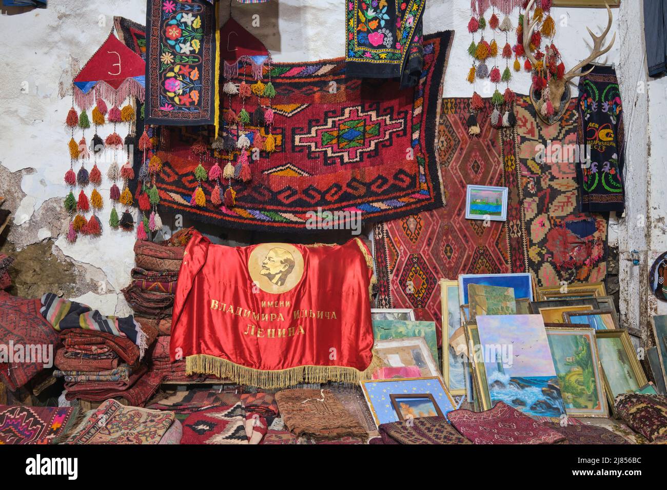 Vecchi tappeti e una vecchia bandiera rossa del leader sovietico Vladimir Lenin. Presso il mercato di Yangiobod Bozor a Tashkent, Uzbekistan. Foto Stock