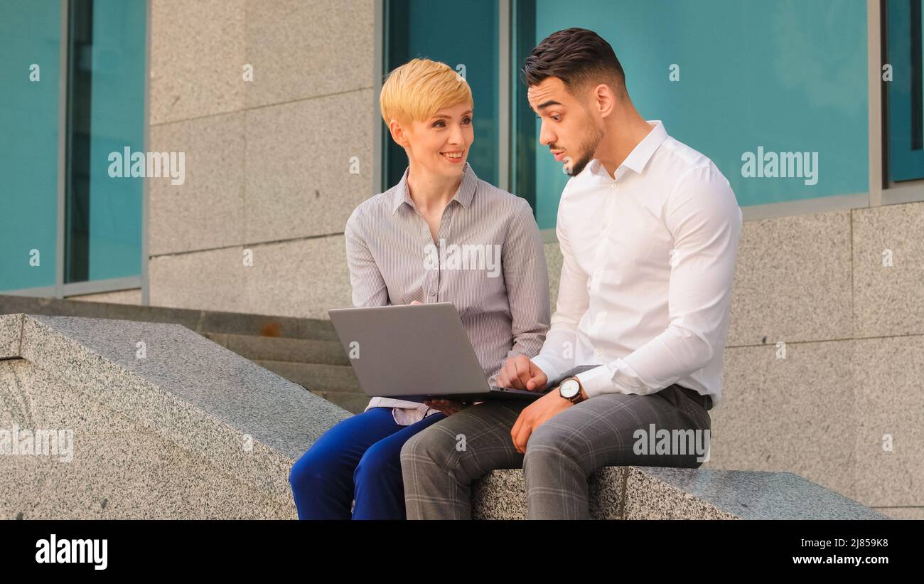 Allegro multietnico coppia colleghi arabo ispanico uomo e donna caucasica in piedi vicino al centro affari in strada all'aperto e. Foto Stock