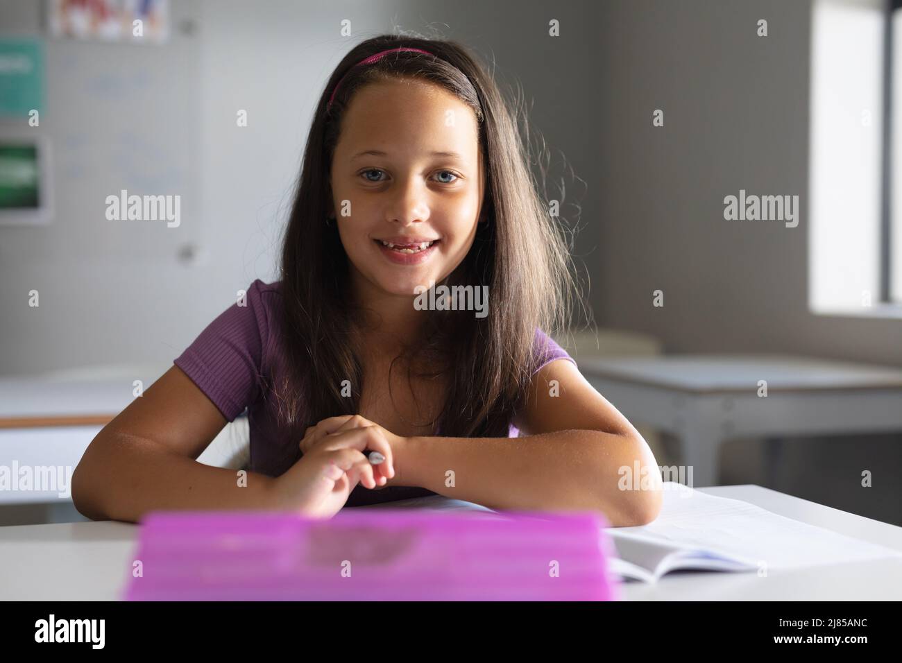 Ritratto di scolaretta caucasica sorridente seduta alla scrivania in classe Foto Stock