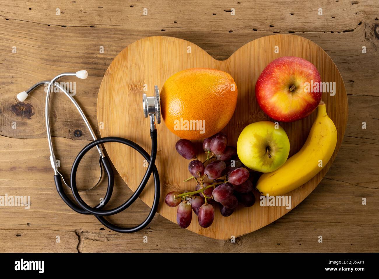 Primo piano di forma a cuore con mele, banana, arancia e uva da stetoscopio su tavola di legno Foto Stock