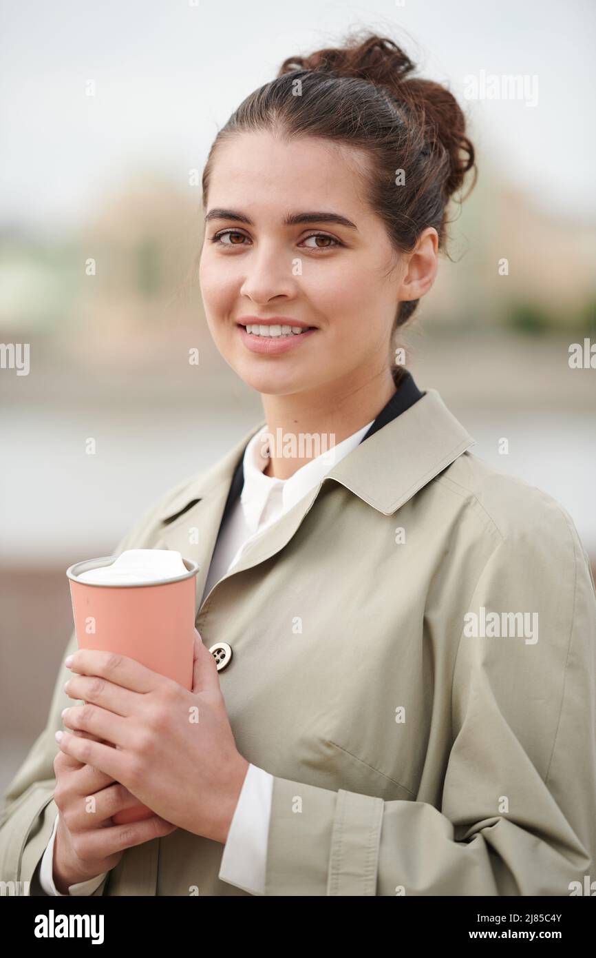 Ritratto di positiva bella giovane donna in autunno cappotto bere caffè caldo da thermos tazza all'aperto Foto Stock
