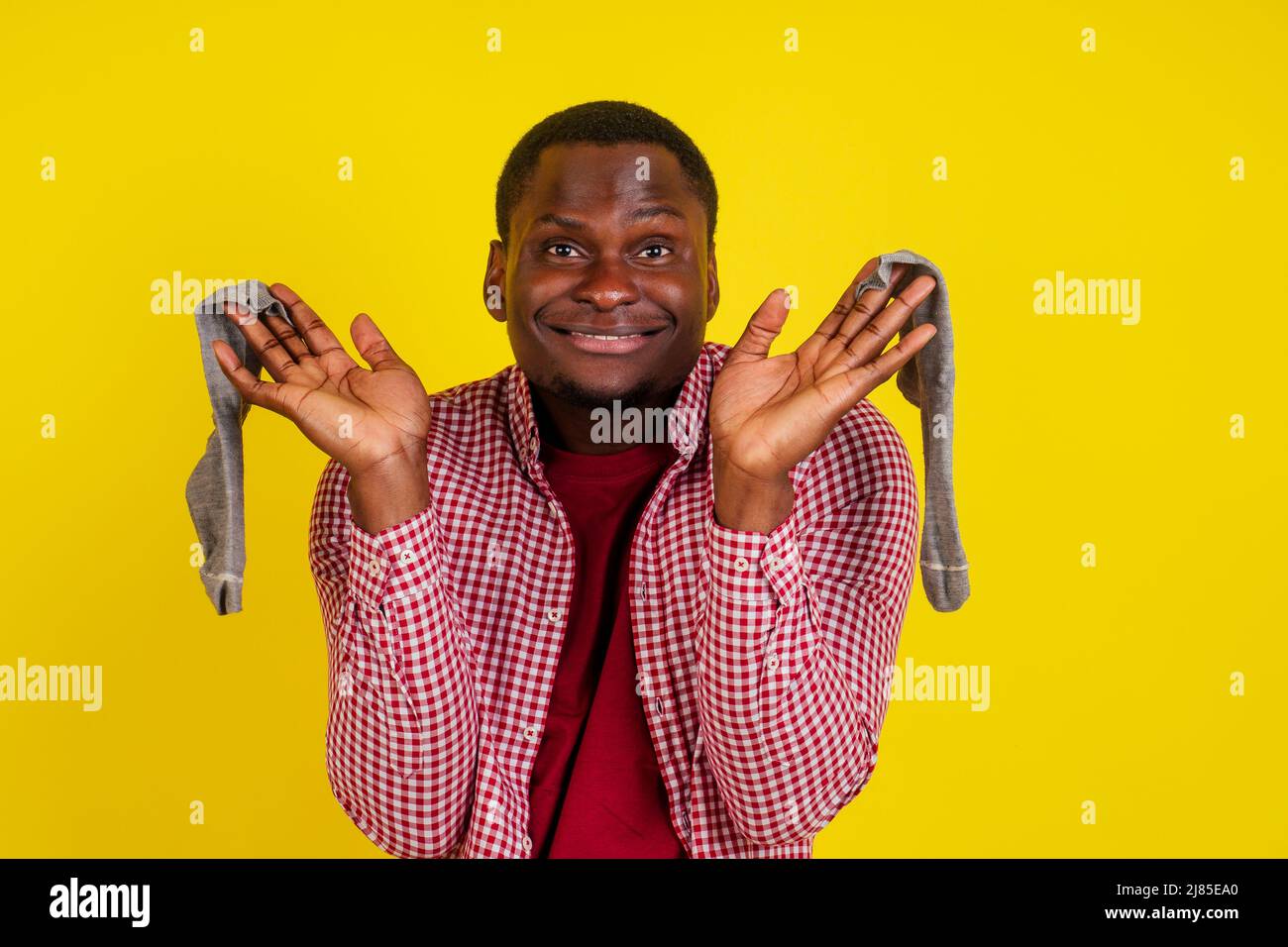 L'uomo afro-americano insoddisfatto chiude il naso, sente di calzini cattivo odore, indossa casual t-shirt rossa in studio sfondo giallo Foto Stock