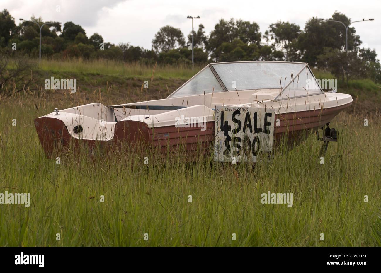 Barca in vendita per $500 su erba verge di strada urbana sulla Gold Coast, Australia. Imbarcazione a motore senza motore. Clima grigio umido. Foto Stock