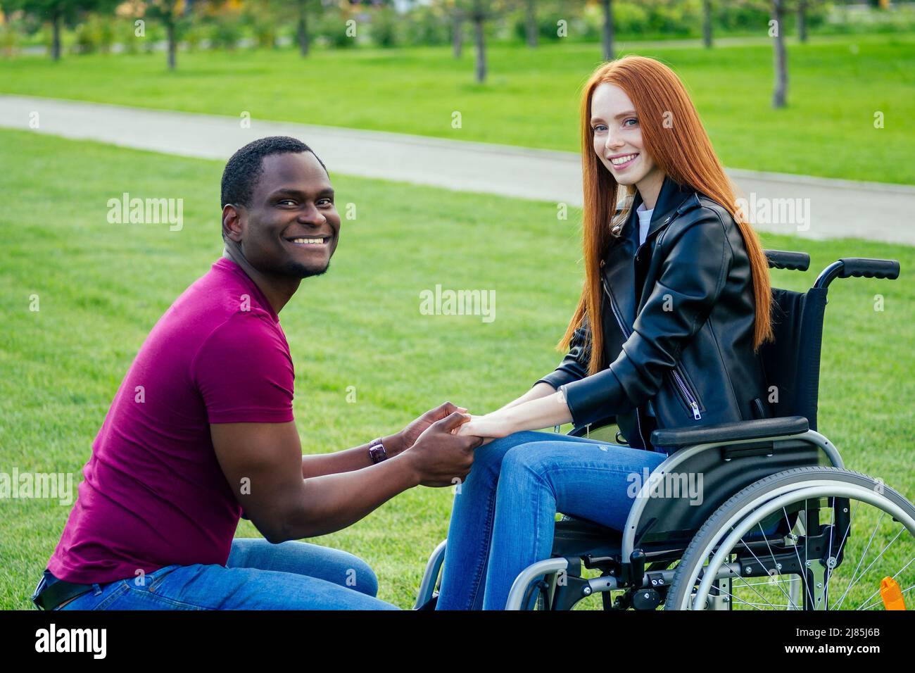 afro american uomo matrimonio proposta dando un anello al suo rosso zenzero girlfriend.she seduta su sedia ruota e sorpreso e stupito Foto Stock