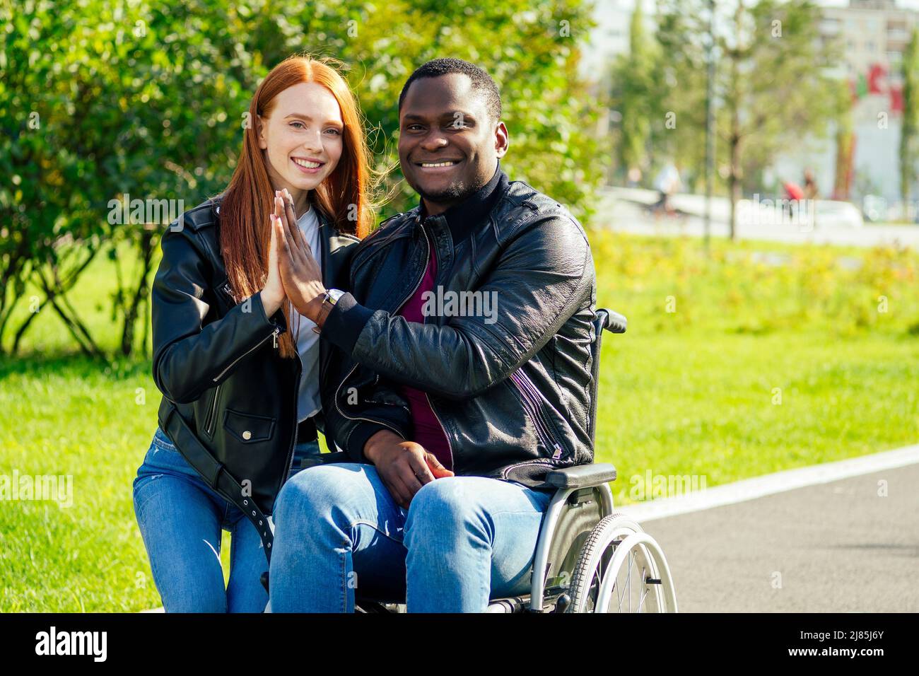 afro american uomo seduto su sedia a rotelle, la sua ragazza zenzero rossa girello rolling nel parco autunnale. avendo data romantica Foto Stock