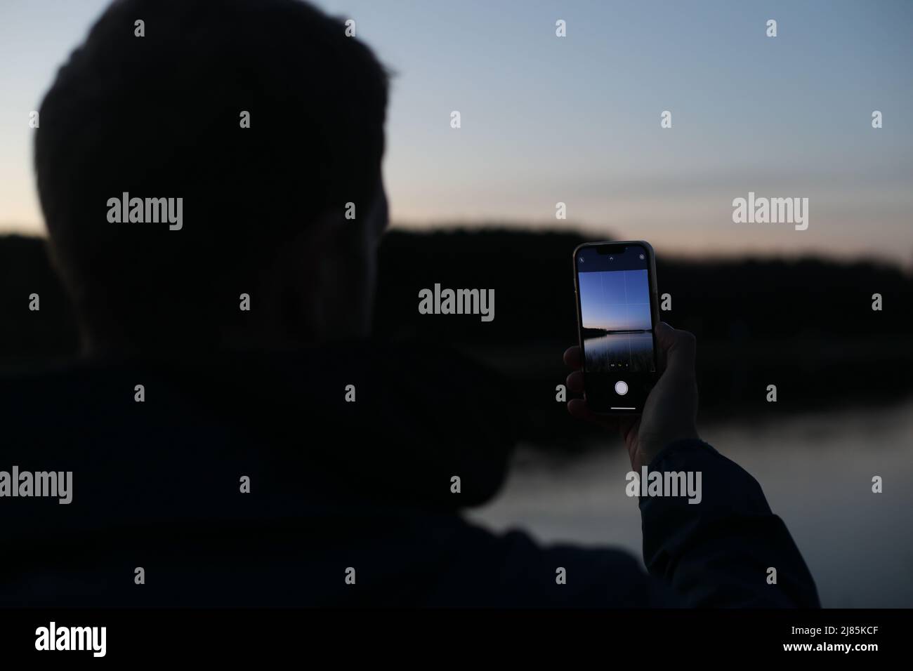 tenere in mano lo smartphone e scattare foto del bellissimo tramonto Foto Stock